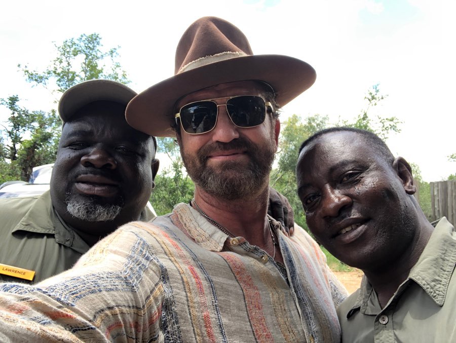 Gerard Butler sitting on the ground playing and laughing with kids during a charitable community visit in Liberia, Africa