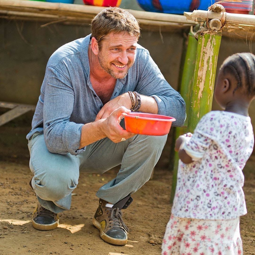 Gerard Butler carrying boxes of medical aid and educational supplies during a humanitarian mission